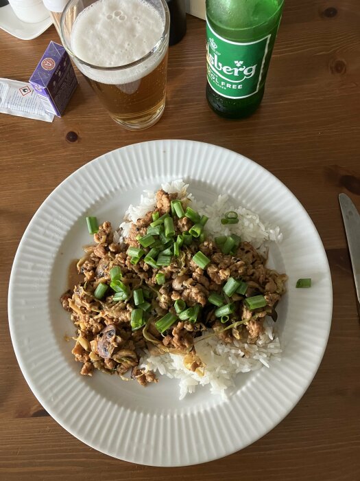 Ett tallrik med ris och wokad kyckling toppad med grön lök, ett glas öl, och en Carlsberg alkoholfri flaska.