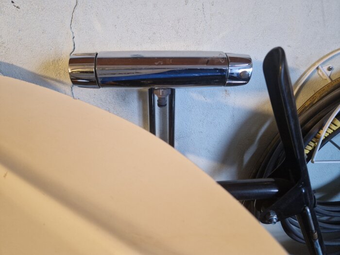 Väggmonterad handdukstork, skugga, del av stol och cykeldäck syns i opersonligt utrymme.