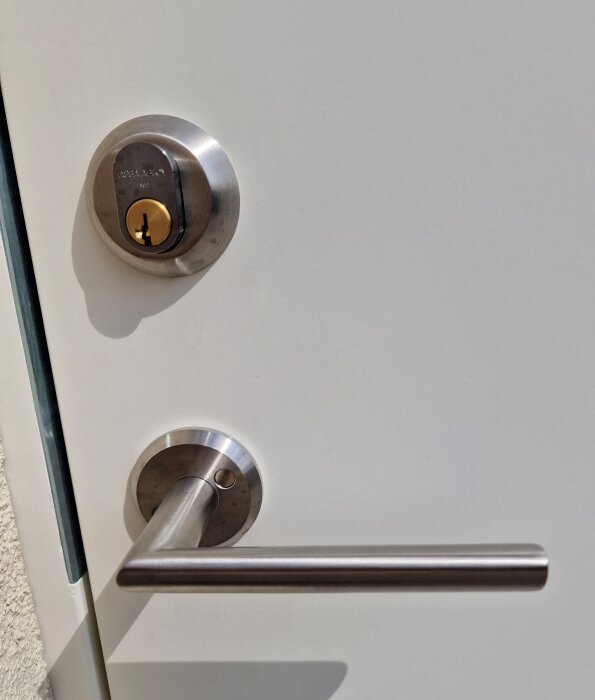 Vit dörr med metallhandtag och låscylinder i dagsljus.