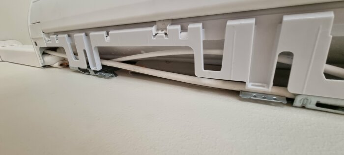 Värmepumpens inomhusenhet, delvis urtagen frontpanel, exponerade rör och kablar, under underhåll eller reparation.