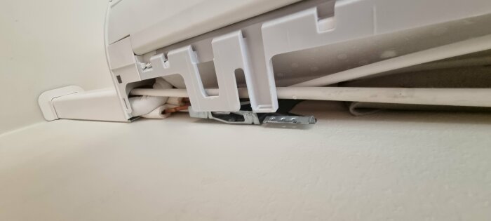 Kabelkanal med öppen lucka och utsatta kablar på en vit vägg.