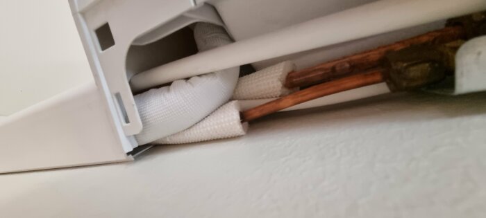 Inre del av värmeelement med kopparrör, isolering, fixeringsdetaljer; blick vinkel mot taket.