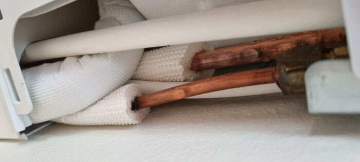 Vattenledningar och isolering inuti en värmeelementskydd. Fokus på kopparör och termiskt material.