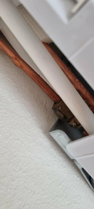 Bild av radiatoranslutning, kopparrör och vägg med synlig isolering och fästelement.