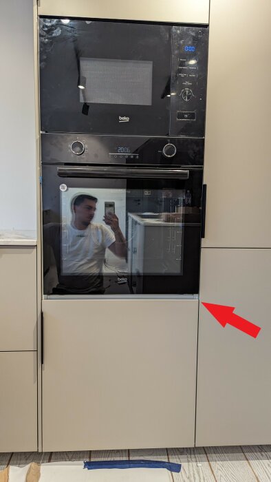 Köksskåp med inbyggda ugnar och mikrovågsugn, reflexionen visar en person som tar en selfie.
