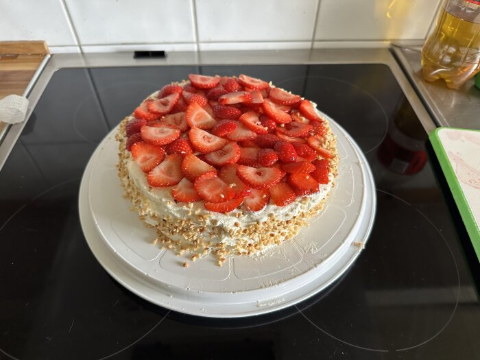 Tårta med jordgubbar och hackade nötter på ett köksbord.