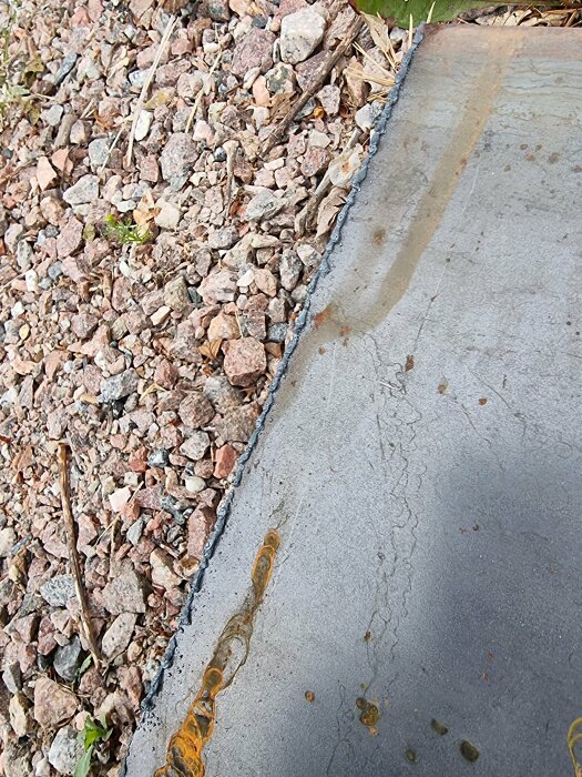 Bild av en trottoarkant med grus och plattor, möjlig vattenskada och smutsiga sprickor.