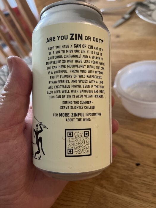 Burk med vinreklam, QR-kod, illustrerad räv med glas, text "ZINFUL" information, hand håller burken.