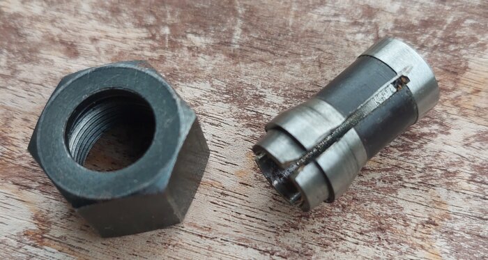 En stor mutter och ett trasigt borrchuck på träbord. Reparationsverktyg eller reservdelar.