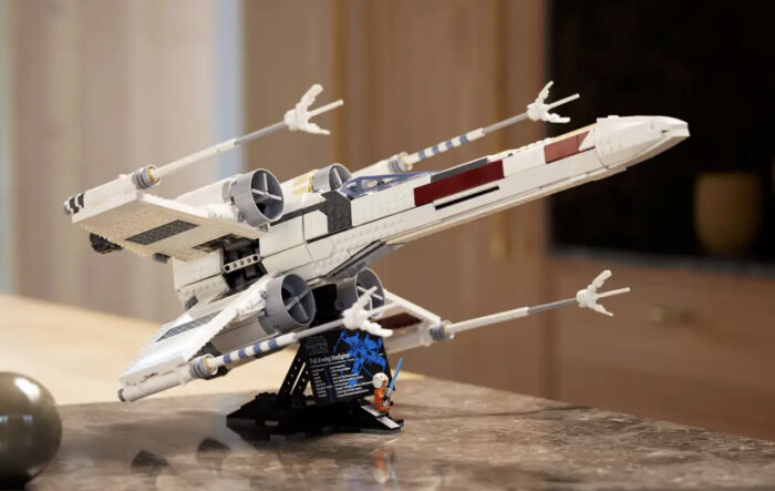 Modell av LEGO X-wing Starfighter med ställ och figur på bänkskiva.