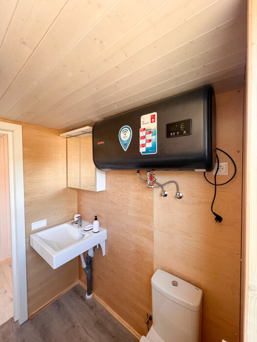 Inomhusbild av ett litet badrum med handfat, toalett och väggmonterad vattenvärmare.