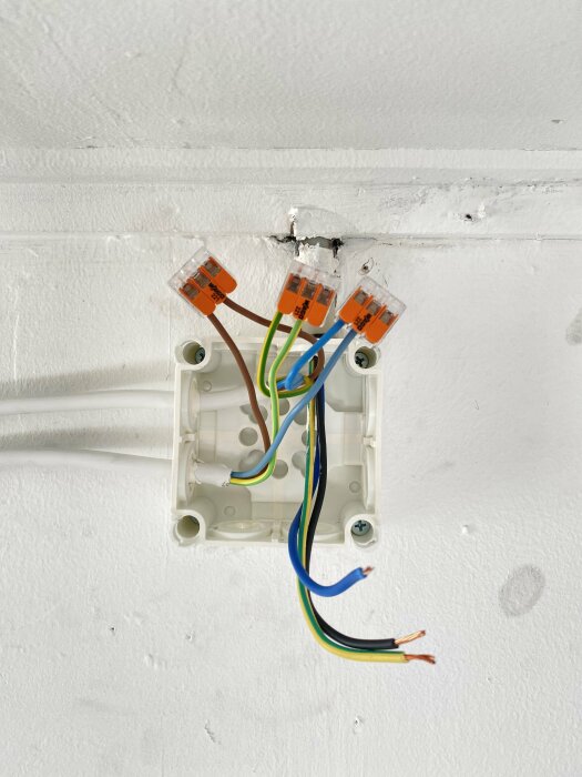 Elektriska kablar och anslutningar i dosa på vit vägg, installationsarbete, osäker, oskyddad, ofärdig elektrikinstallation.