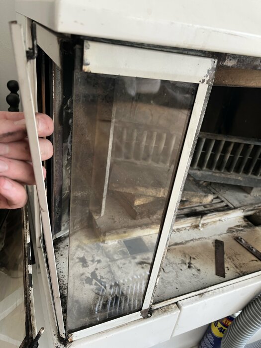 Nedsmutsad ugnslucka med rester av brända material, rök- och sotskador synliga; behöver rengöring.