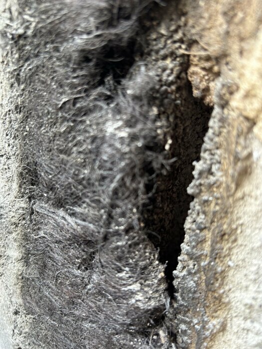 Närbild av textur, möjligen isoleringsmaterial eller filt, gråsvart färg, fuzzy yta, oskarpt i bakgrunden.