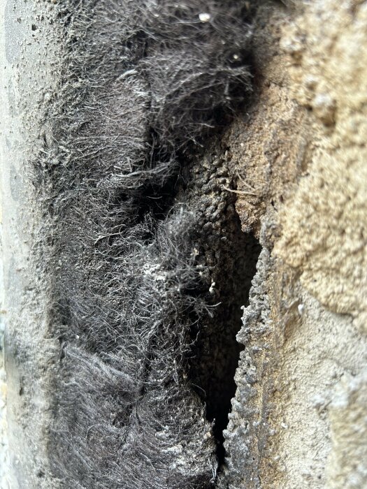 Textur av damm och smuts i ventilationsöppning eller liknande, med närbild på fiberrika ansamlingar.