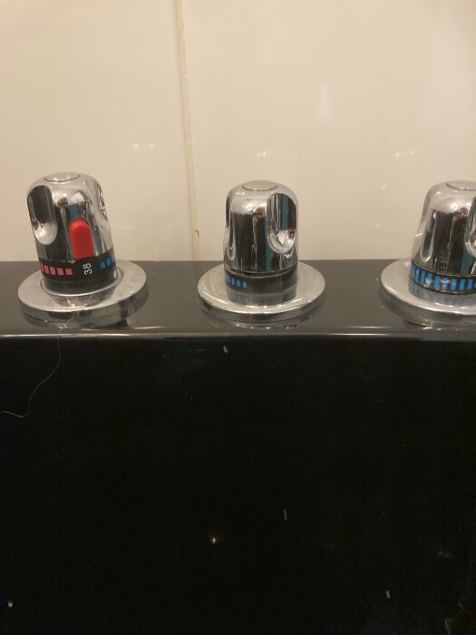 Tre vattenkranar med markerade temperaturinställningar på marmorbänk mot vit vägg.