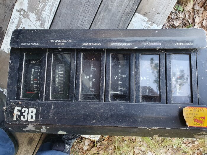 Gammal anordning med mätinstrument, kanske för tåg eller tunga fordon, svensk text, nedsliten, utomhus.