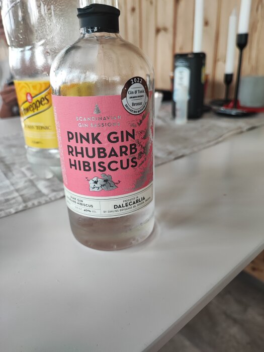 Flaska Pink Gin märkt 'Rhubarb Hibiscus', Schweppes tonic, suddig bakgrund, inomhus, trädetaljer.