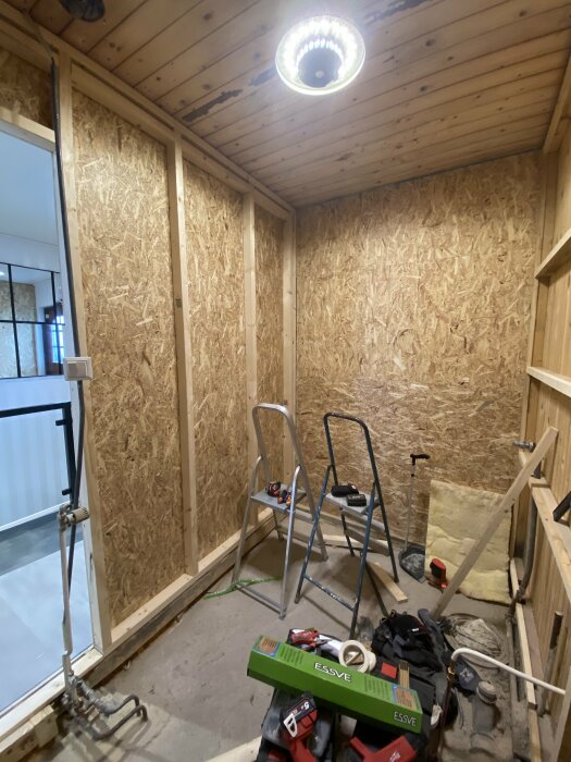 Omfattande rum under renovering med OSB-skivor, byggmaterial och stegar.