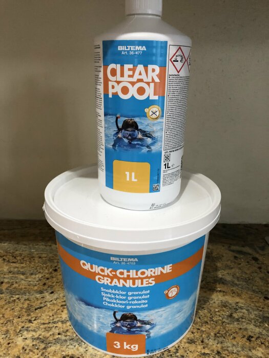 Två Biltema pool-produkter: Clear Pool vätska och Quick-Chlorine Granules, placerade på marmorliknande yta.