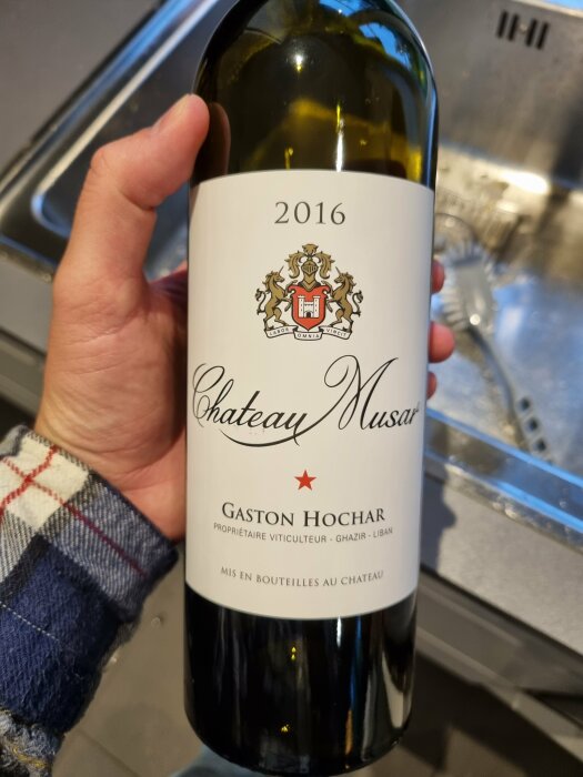 Hand håller Chateau Musar-flaska, årgång 2016, Ghazir-Libanon, i kök.
