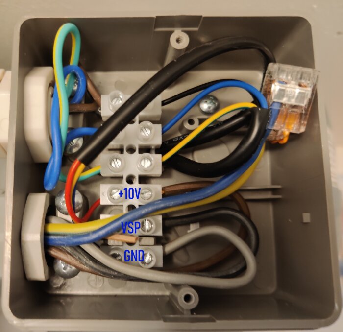 Öppet elektriskt kopplingsdosa med märkta kablar, anslutningar och en kabelklämma.