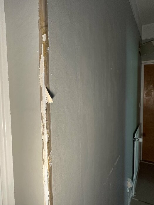Skadad vägg med flagnande färg och gips, hörn i en korridor, behöver reparation eller målning.