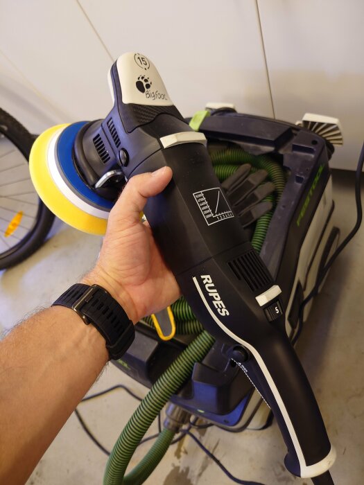 En hand håller en elektrisk polermaskin ovanpå en verktygslåda i ett garage.