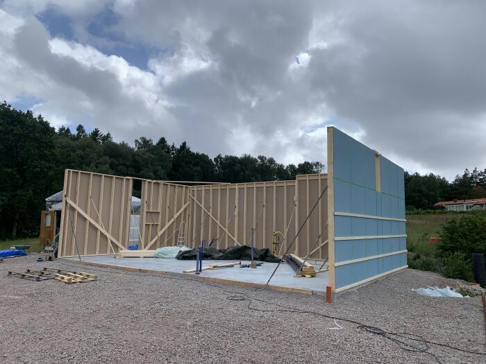 Husbygge i trästomme, isoleringsplattor, mulen himmel, byggarbetsplats, skog i bakgrunden.