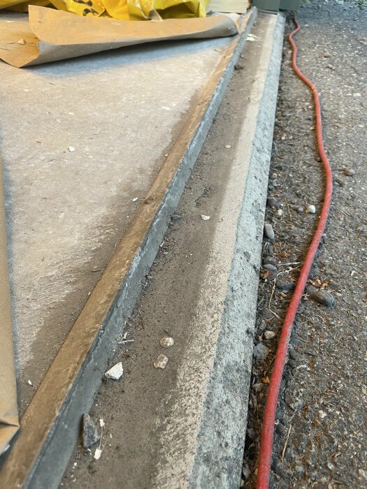 Betongyta, röd slang, brunt papper, byggdetaljer, utomhusmiljö, skräp.