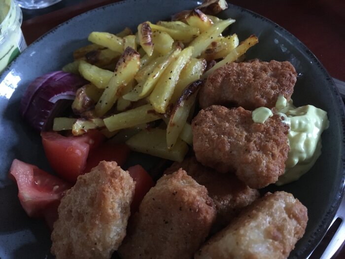 Tallrik med nuggets, stekt potatis, tomat, rödlök och majs. Hemlagad måltid med dippsås.