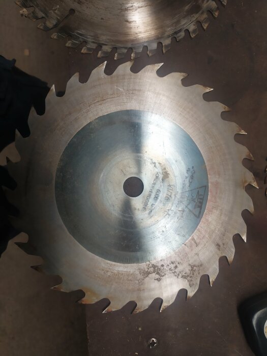 En stor cirkulärt sågblad med tänder ligger på en arbetsytan, ser använd och industriell ut.