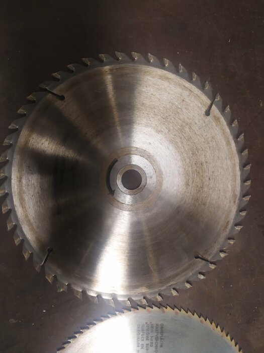 Cirkelsågblad, tandade, metall, ligger på en sliten yta, verktyg, skärverktyg, två blad, olika storlekar, industriell.