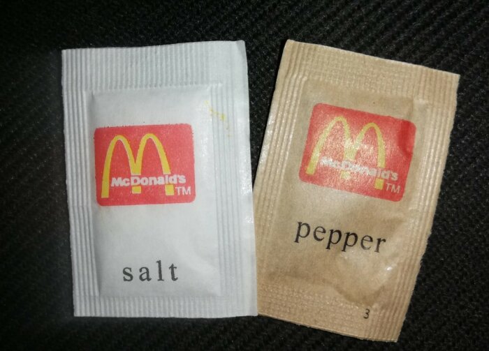 Salt- och pepparpåsar från McDonald's på mörk bakgrund.