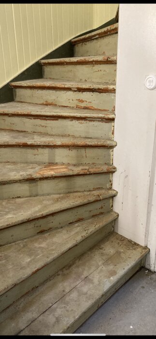 Gammal trappa inomhus, slitna steg med rost och avskalad färg, behov av renovering.
