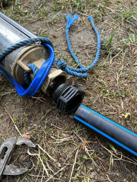 Vattenpump, slang, tång och trasigt rep på gräs- och jordunderlag.