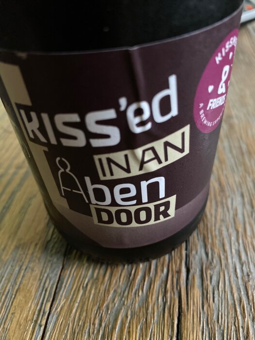 Brun pappersmugg med text, på träbord. Delvis synligt ord antyder att något "kissat" på muggen. Humoristiskt budskap.