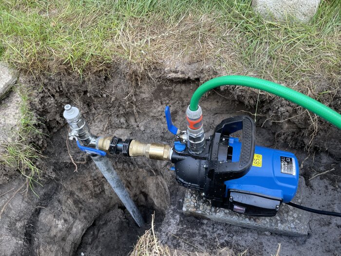 Blå vattenpump med slangar i grävd grop, dränering eller vattenförflyttning utomhus.