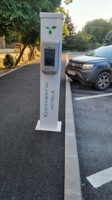 Laddningsstation för elbil vid Continental hotel, asfalterad parkeringsplats, skymning, träd, del av bil synlig.