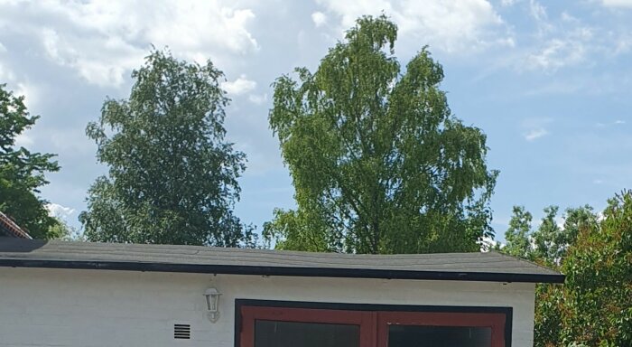 Vit byggnad med röda accenter, träd i bakgrunden, molnig himmel ovanför.