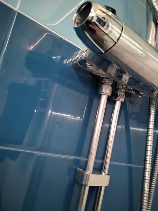Kromad duschblandare och rör mot blå kakelvägg i badrum.