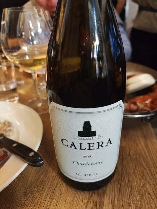 En flaska Calera Chardonnay 2018 vid en måltid med vin glas och rätter skymtar.