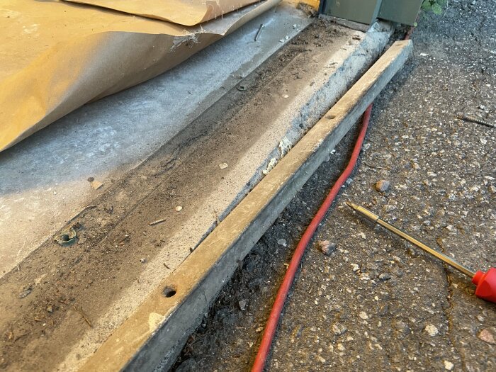 Byggarbetsplats med betongfundament, röd kabel, skruvmejsel och brunt skyddspapper.