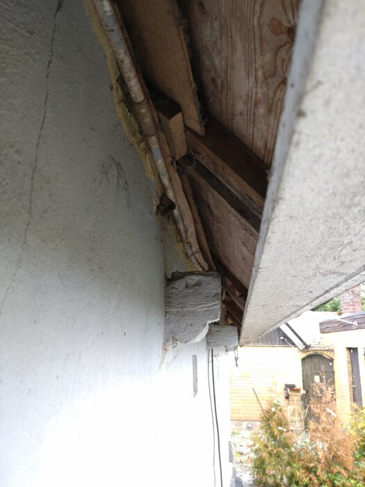 Slitet hörn av tak med synliga träbjälkar och rör, i behov av reparation.