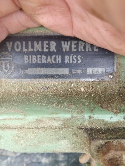 Etikett från "Vollmer Werke Biberach Riss", dammigt maskinerimärke, grönt, handen håller det, text och symboler.