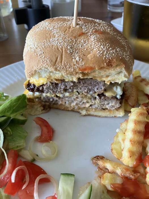 Hamburgare med ostdrypande biff och frön på brödet; sallad, lök, tomat bredvid; crinkle-cut pommes frites; ölglas.