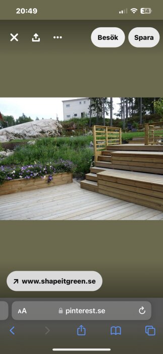 Trädäck med planteringar, trappa, staket och hus i bakgrunden. Gröna trädgårdselement, stenig kulle, blommor.