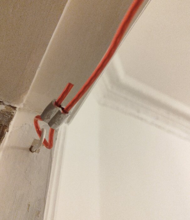 Röd kabel fastklämd med kabelklämma mot en vit vägg.