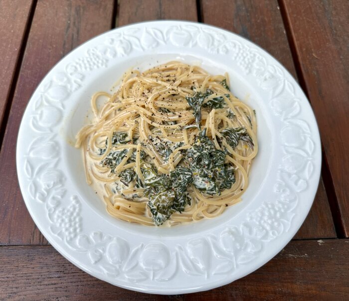 En tallrik med pasta och gräddig sås, toppad med spenat och kryddor, på träbord.