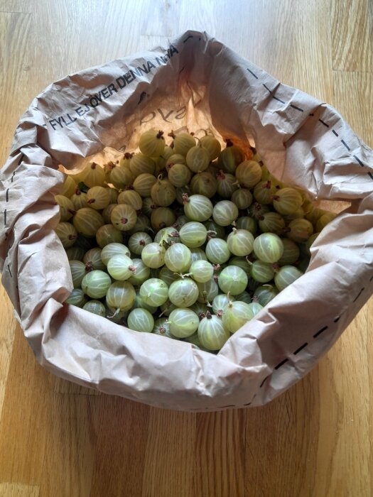 En påse fylld med gröna krusbär på ett träbord, ljus bakgrund, matlagning, hälsa, sommarfrukt.